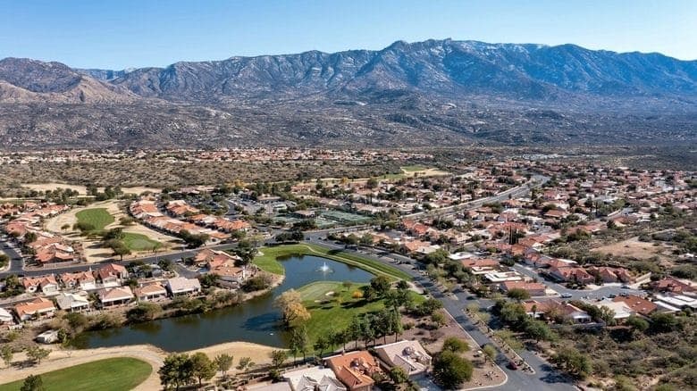 Aerial view of Casas Adobes homes around a golf course pond with mountains in the distance
