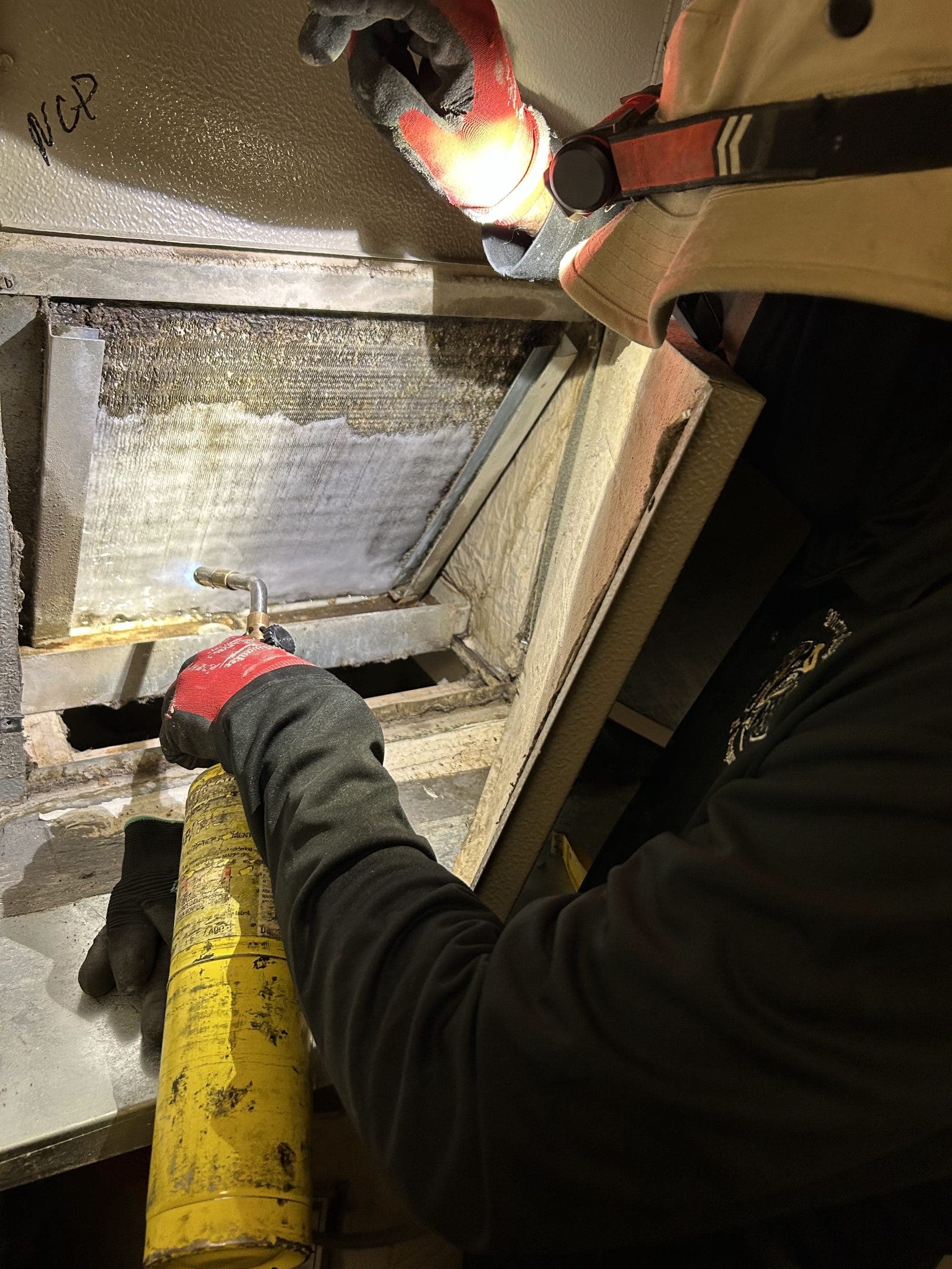 Technician brazing a coil inside an air handler during an HVAC repair