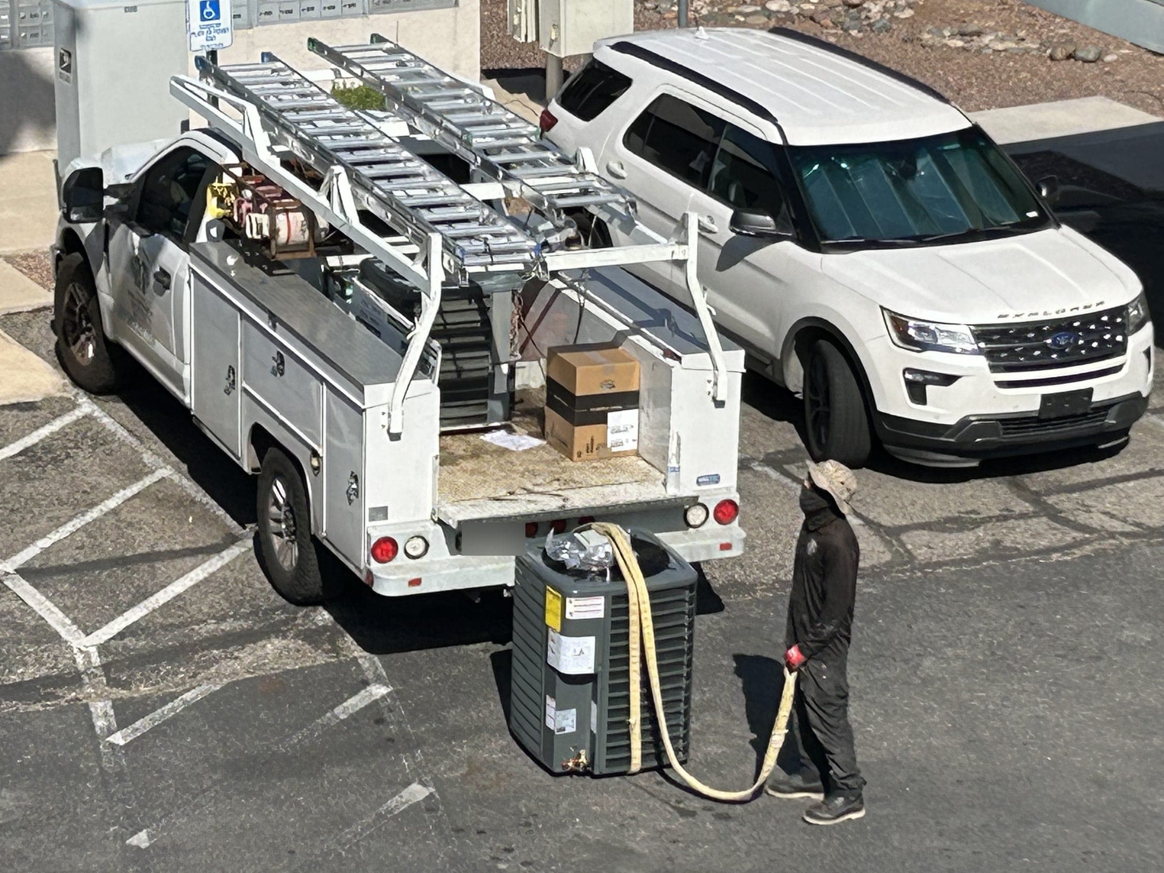 Technician rigging a new condenser behind a Victory Mechanical service truck at an apartment community